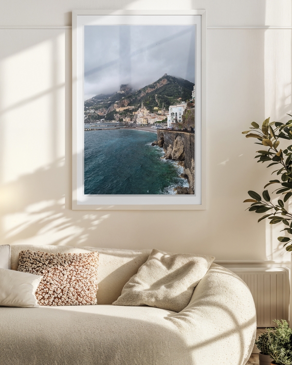 A poster of a Colorful cliffside town overlooking turquoise sea under cloudy sky.
