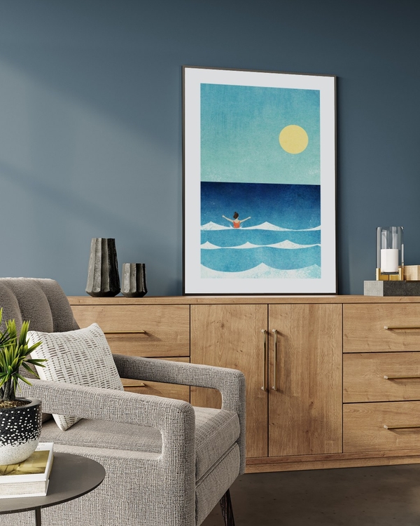 Summer Swim poster in a slim black frame leaning on an oak sideboard against a blue-grey wall