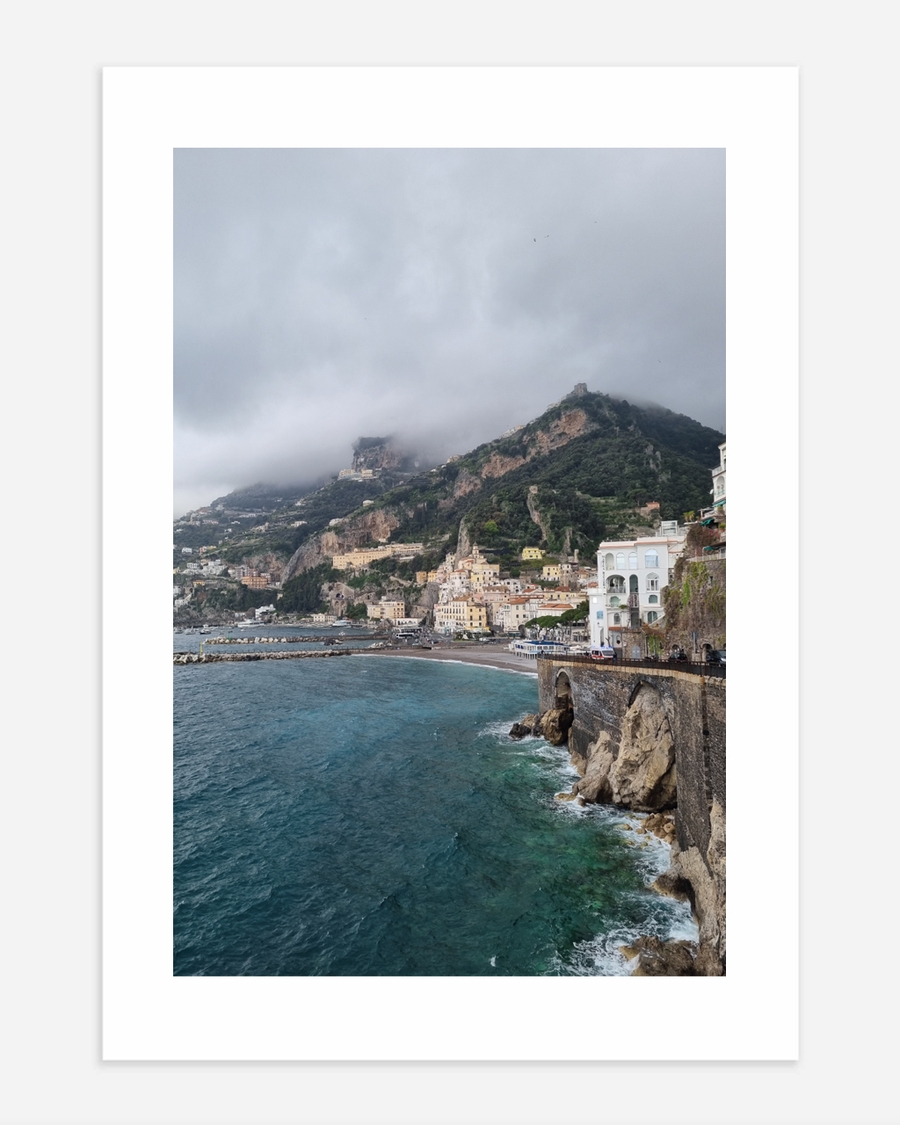 A poster of a Colorful cliffside town overlooking turquoise sea under cloudy sky.