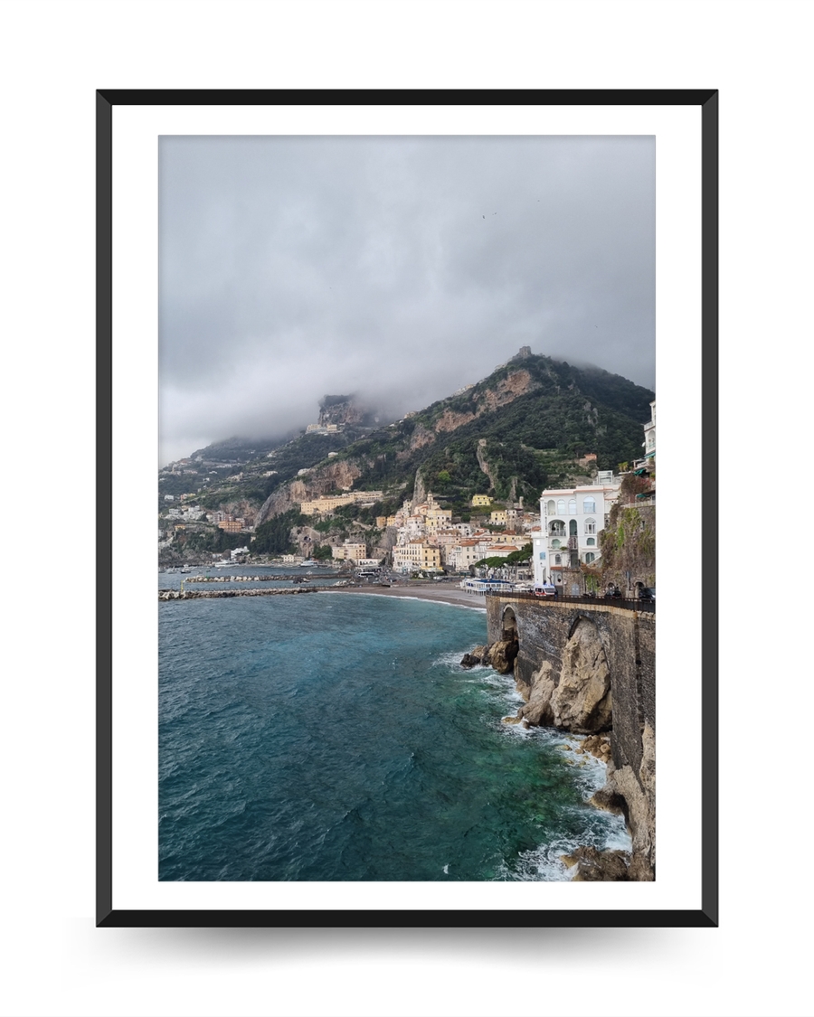 A poster of a Colorful cliffside town overlooking turquoise sea under cloudy sky.