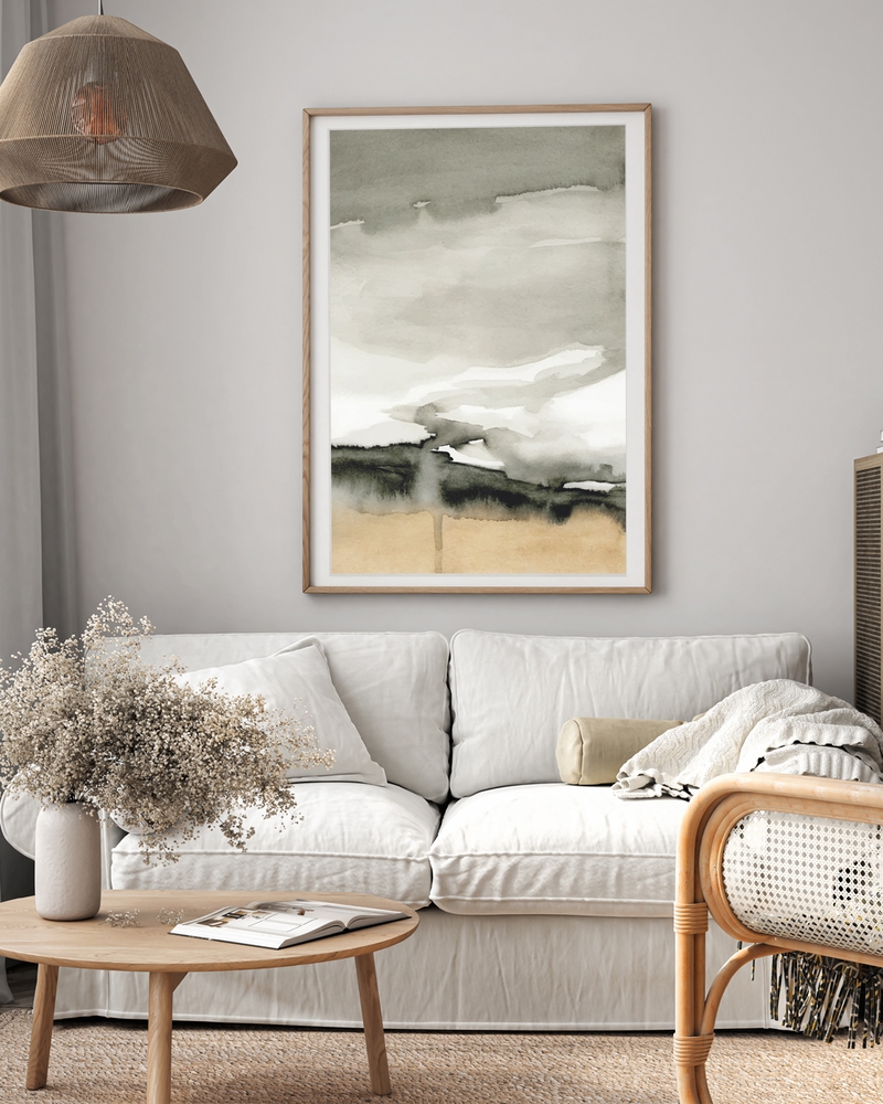 Gray and sand watercolor landscape poster in a light wood frame above a white sofa in a calm, neutral living room