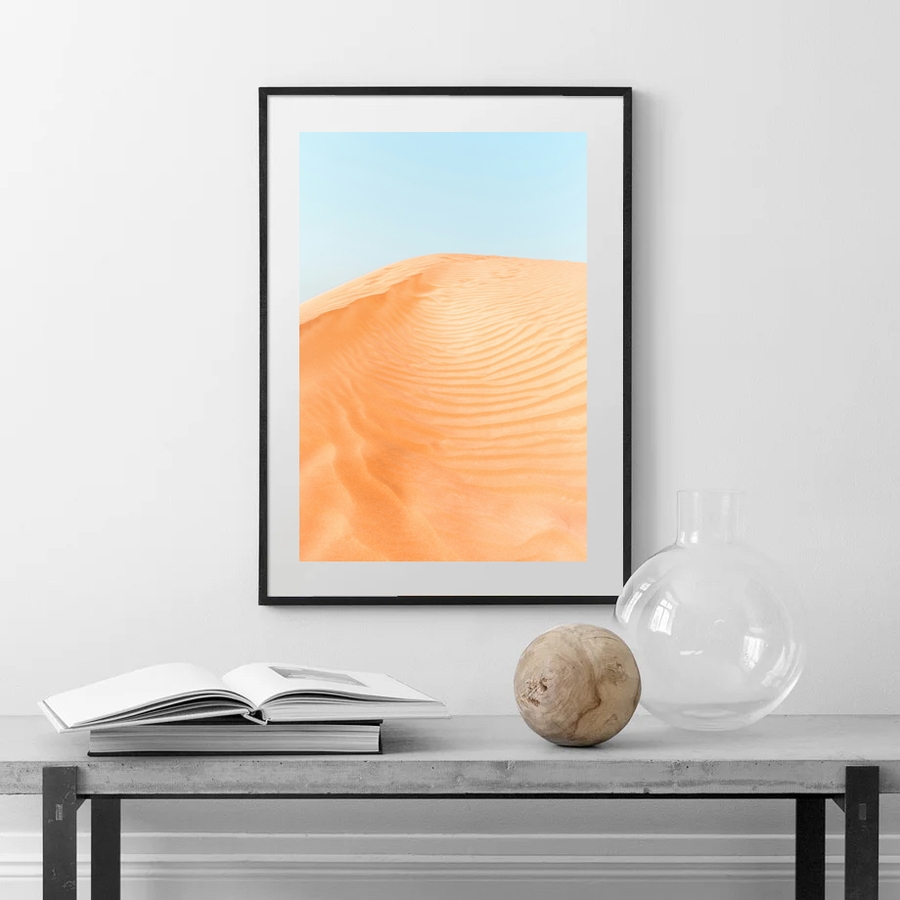 An orange desert with a blue sky poster hanged on a wall over a table.