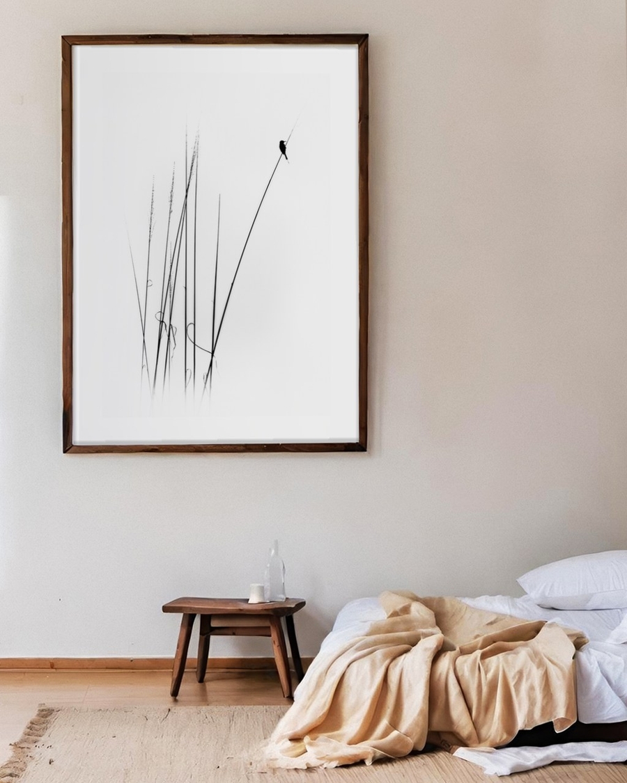 Bird on Reeds poster in a large dark wood frame above a wooden stool in a calm bedroom