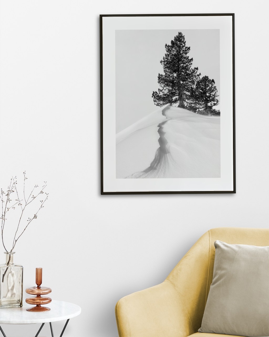 Snowdrift Pines poster in a slim black frame on a white wall above a yellow armchair