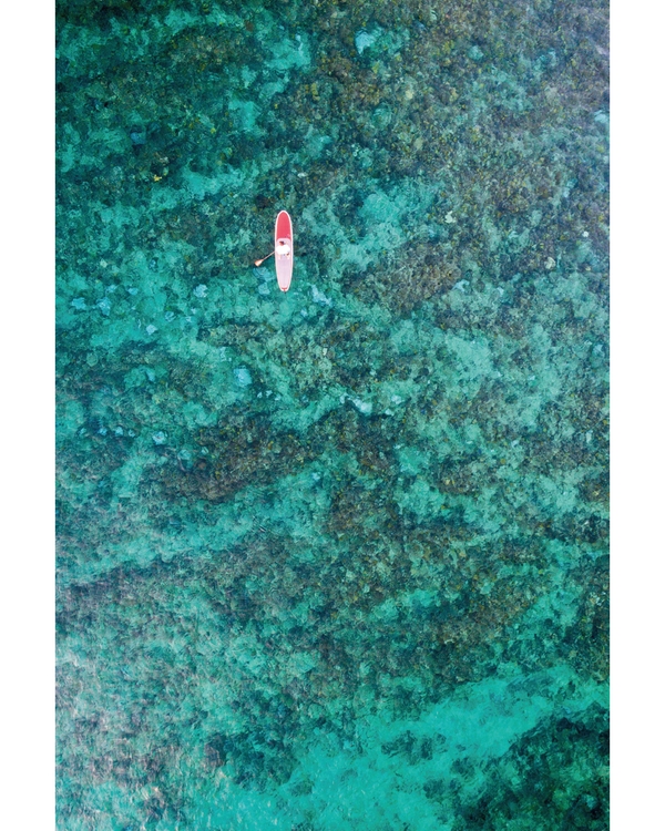 Aerial paddleboarder floating above turquoise coral reef