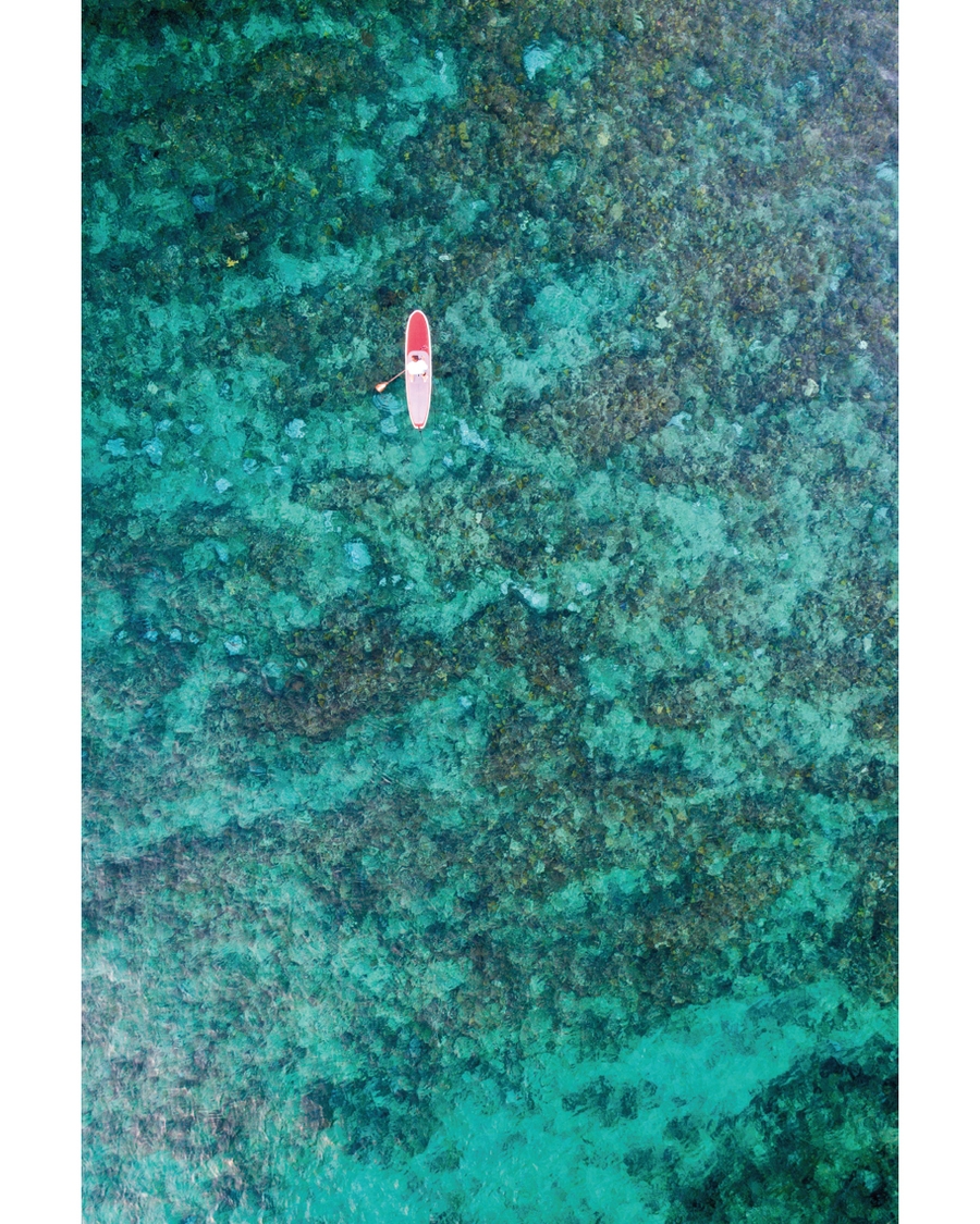 Aerial paddleboarder floating above turquoise coral reef