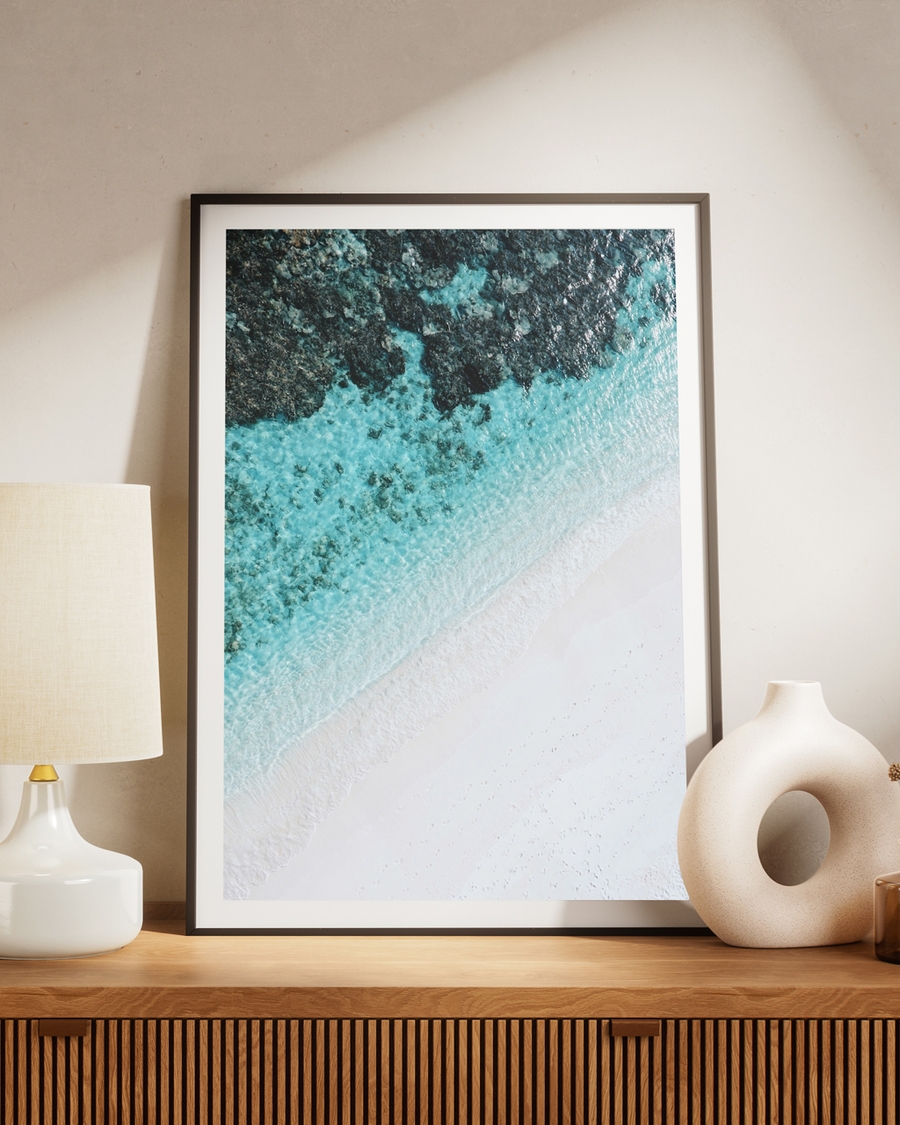 A poster of a tranquil aerial view of turquoise waves meeting soft white sand on a brown table