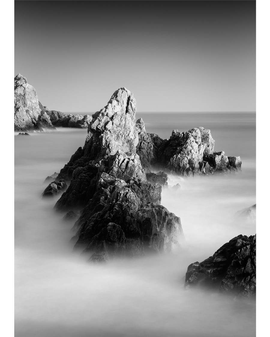 Black-and-white rocky coastline with misty ocean waves