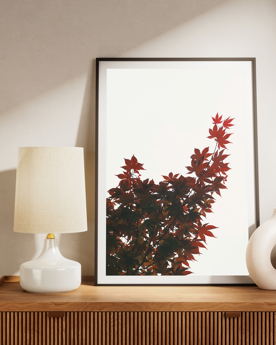 Poster of a crimson maple tree leaves over a brown table next to a light lamp