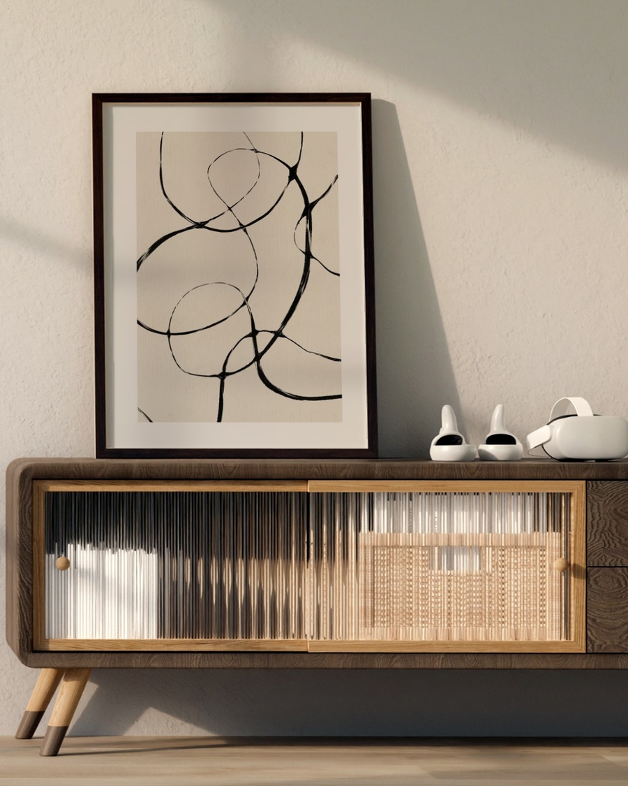 Ink Loops poster in a dark wood frame leaning on a mid-century sideboard against a warm beige wall