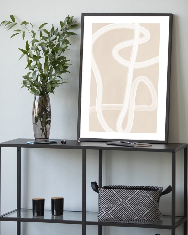 Ivory Ribbon Path poster in a slim black frame leaning on a metal console table with greenery