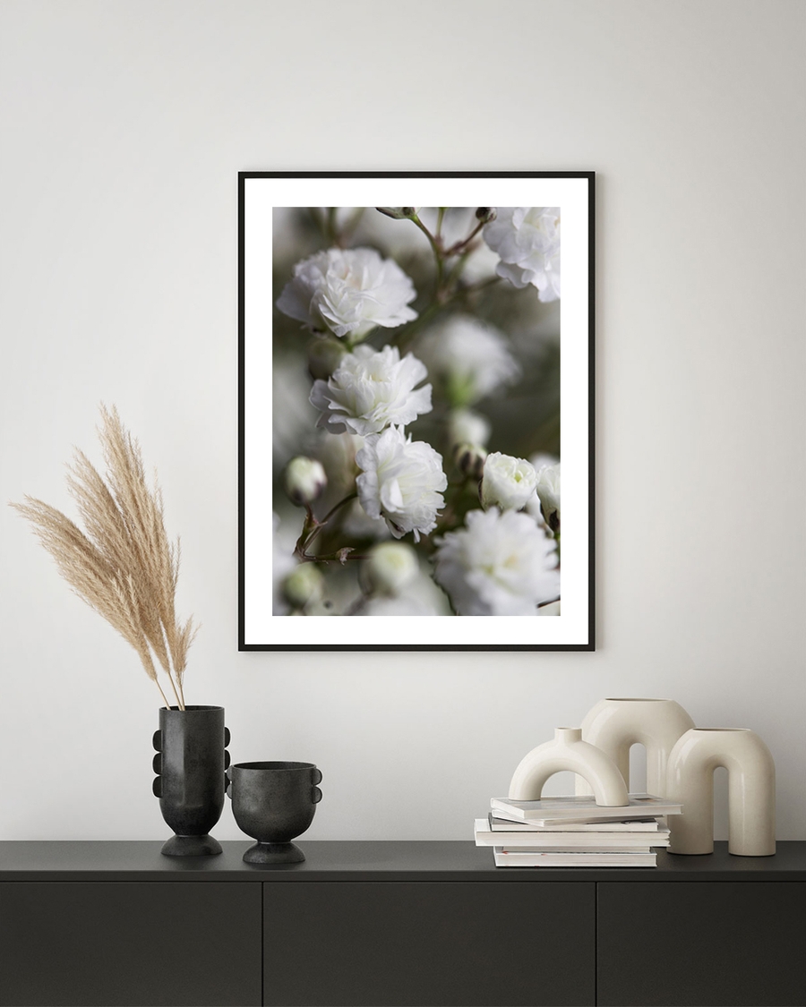 A framed poster of white flowers on tree hanged over a table