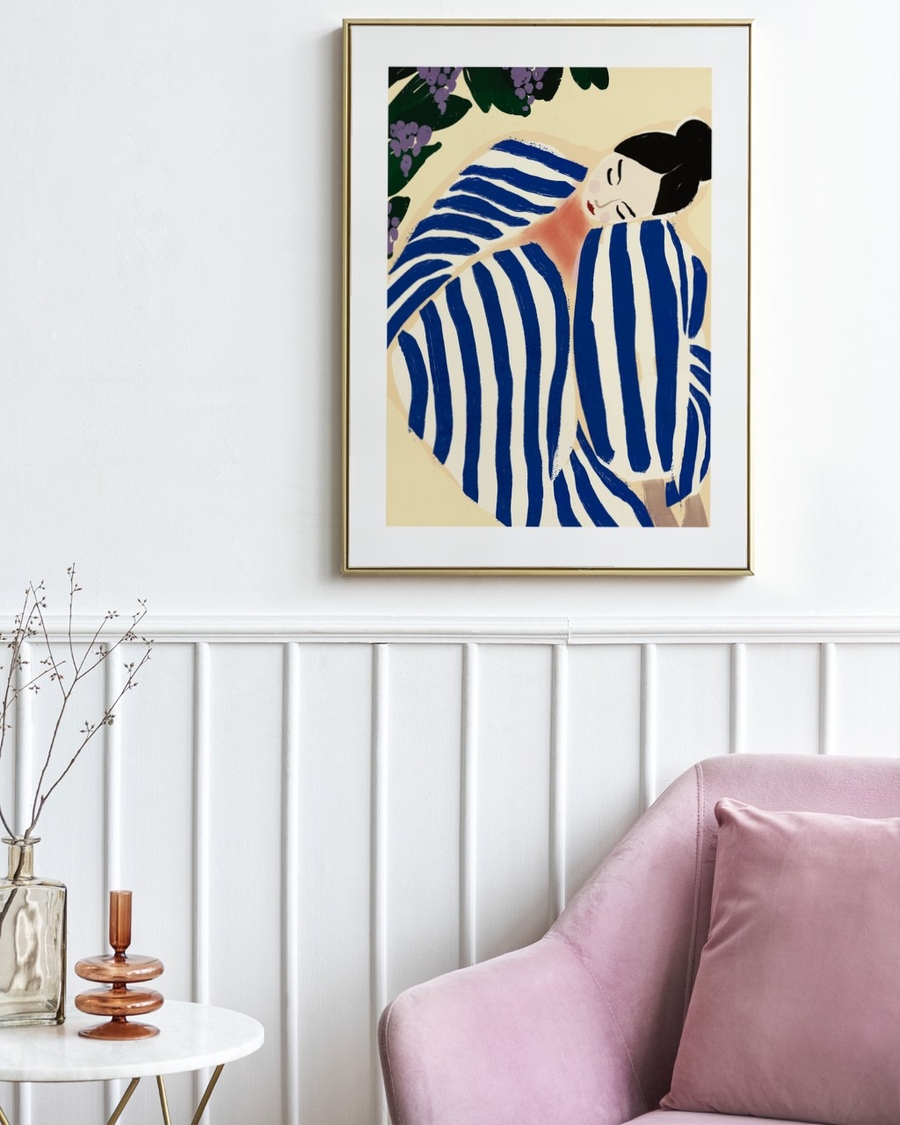 Striped Siesta poster in a slim gold frame above white panelling beside a pink velvet sofa
