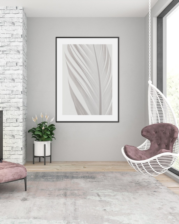 White Plume poster in a slim black frame on a grey wall above a potted plant