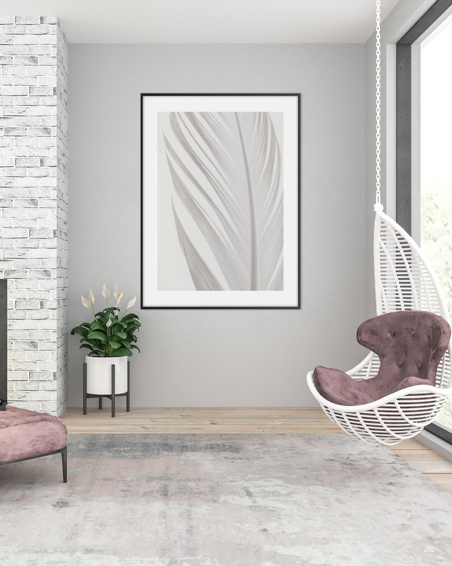White Plume poster in a slim black frame on a grey wall above a potted plant