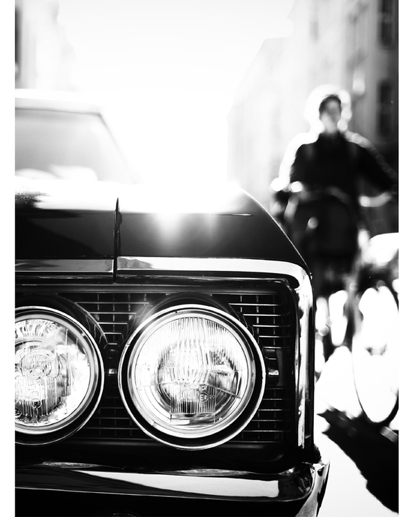 Close-up of classic car headlights with blurred city background.