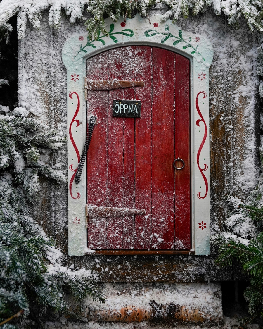 A vibrant red doorway framed by frosted evergreens and Nordic folk art