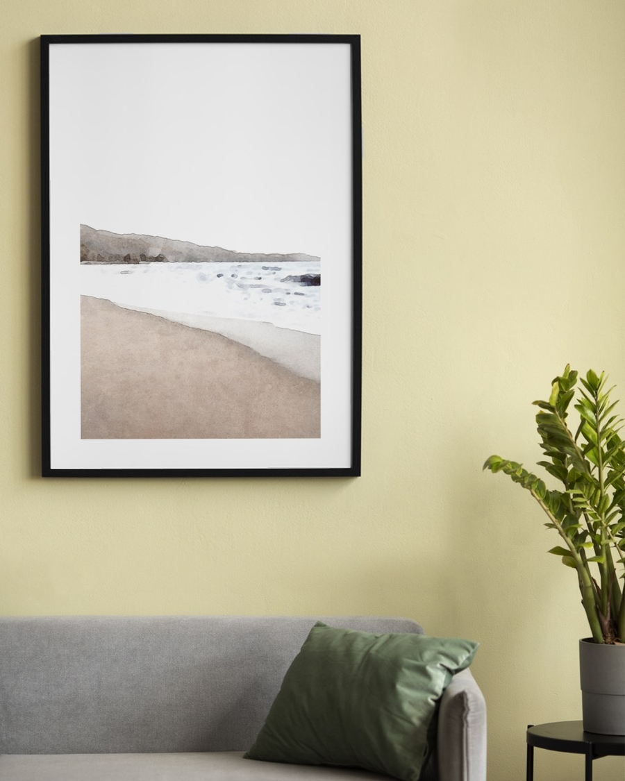 Washed Shoreline poster in a slim black frame on a soft yellow wall above a grey sofa