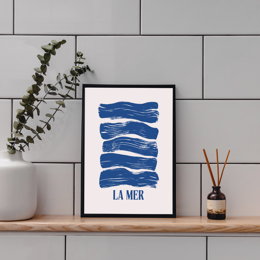 A poster of blue navy waves in a black frame placed on a bathroom shelf