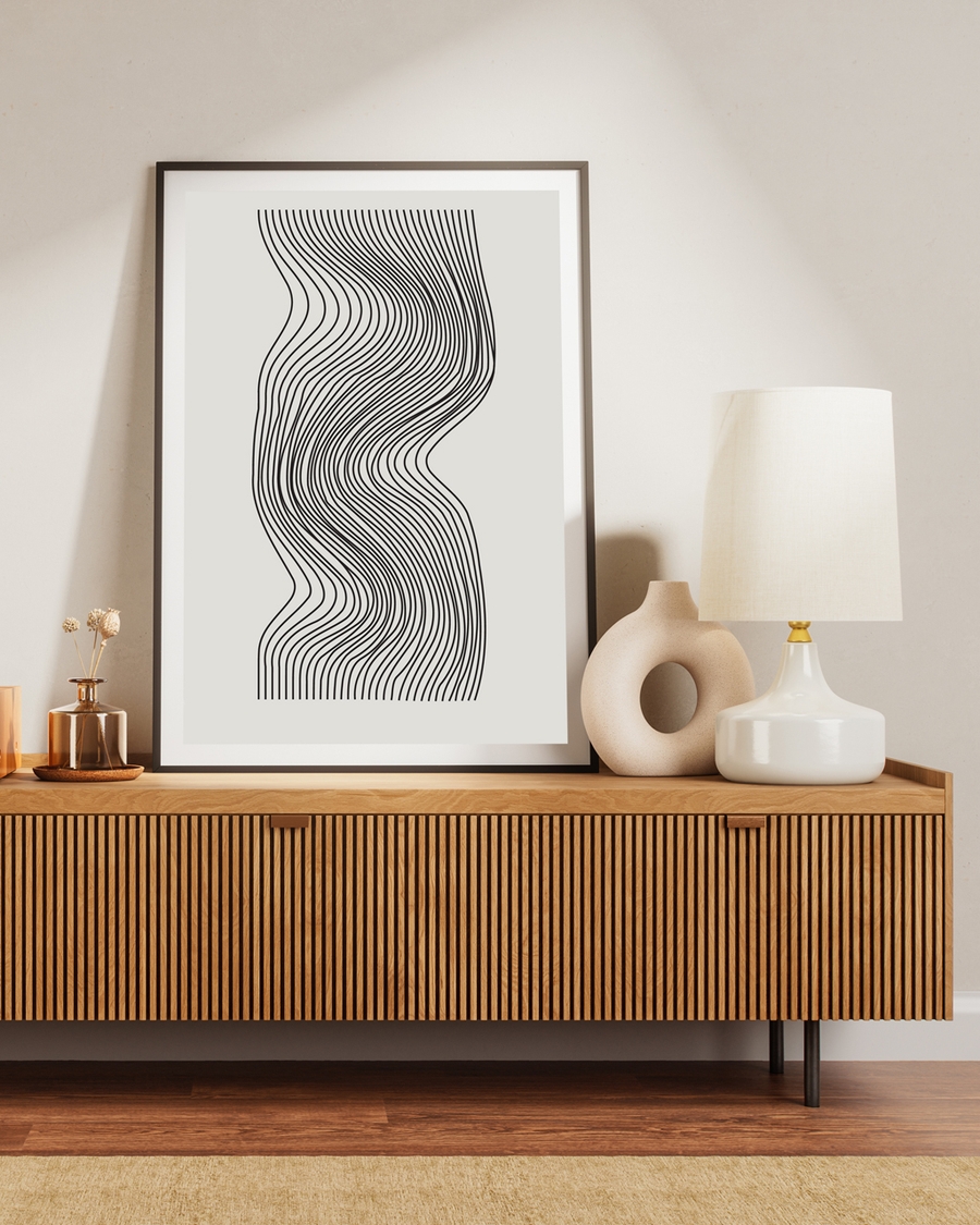 A poster of black lines in a wave form placed over a brown table next to a lamp