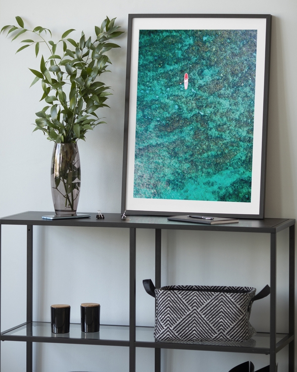 A poster of a Aerial paddleboarder floating above turquoise coral reef
