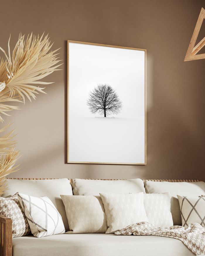 A framed poster of a black lonely tree surrounded by white snow hanged on a brown wall