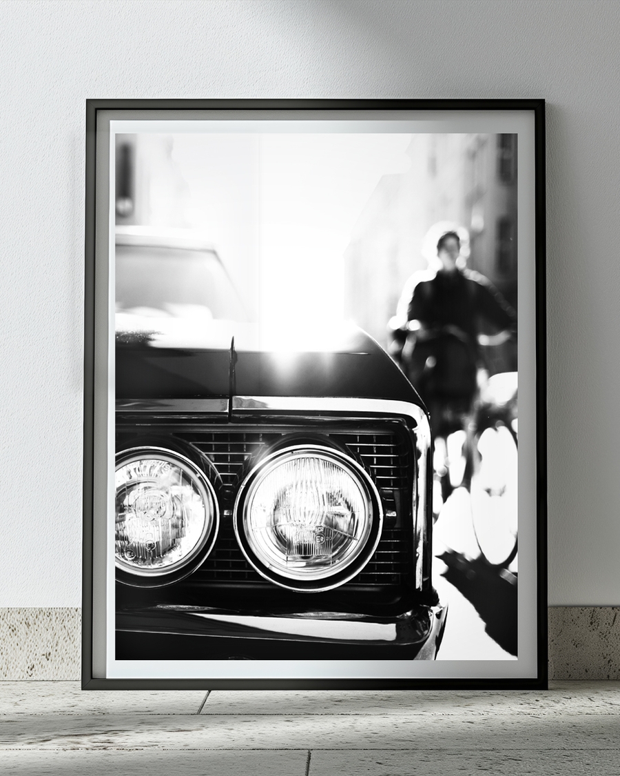 A poster of a Close-up of classic car headlights with blurred city background.