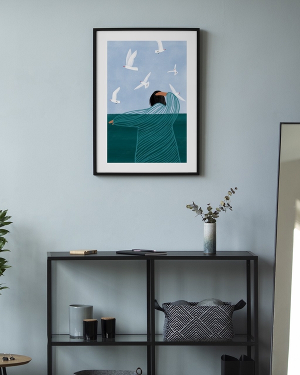 Among the Gulls poster in a slim black frame on a pale blue wall above a black metal console shelf