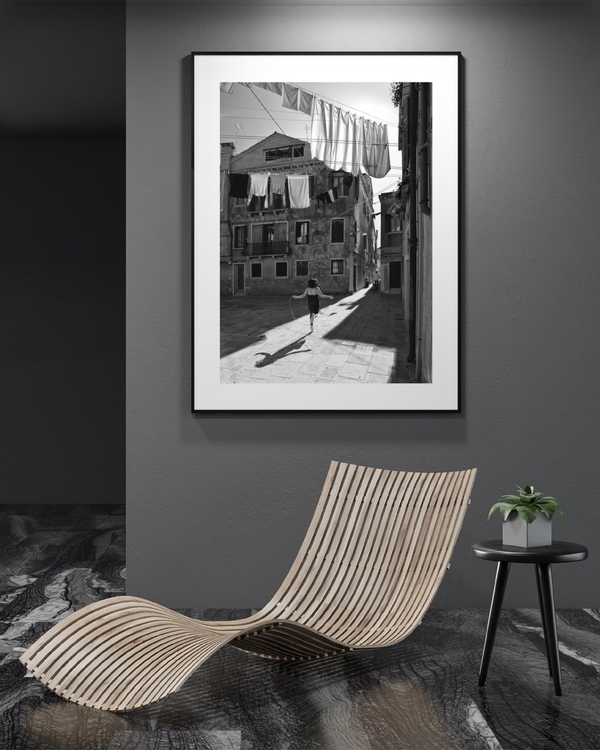 Skipping Through Sunlight poster in a slim black frame on a dark grey wall above a curved wooden lounger