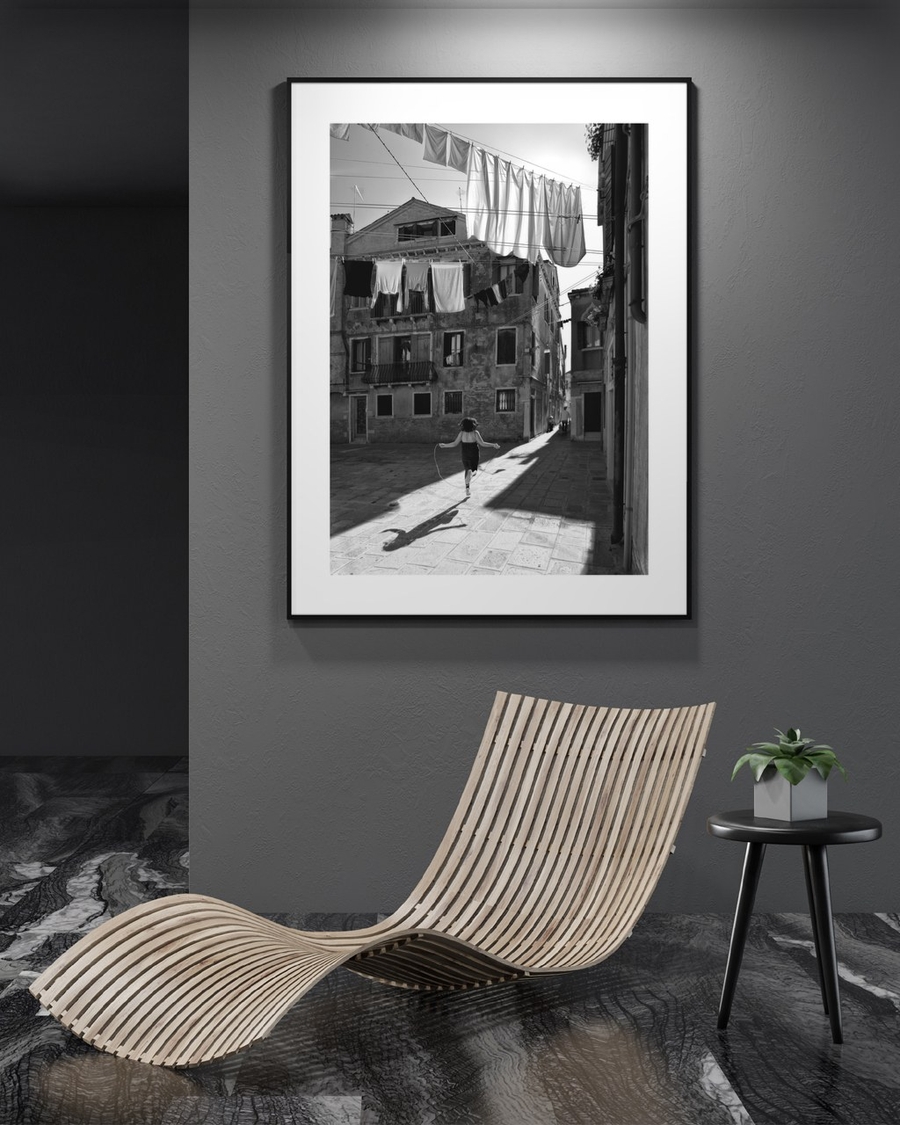 Skipping Through Sunlight poster in a slim black frame on a dark grey wall above a curved wooden lounger