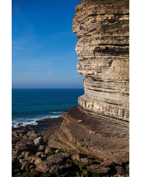 Layered rocky cliff by deep blue ocean waves