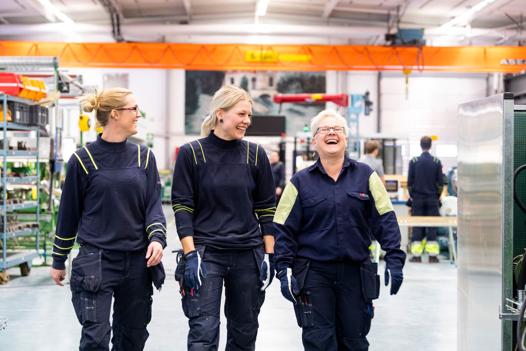 Three colleagues in work clothes laughing as they walk across a factory floor.