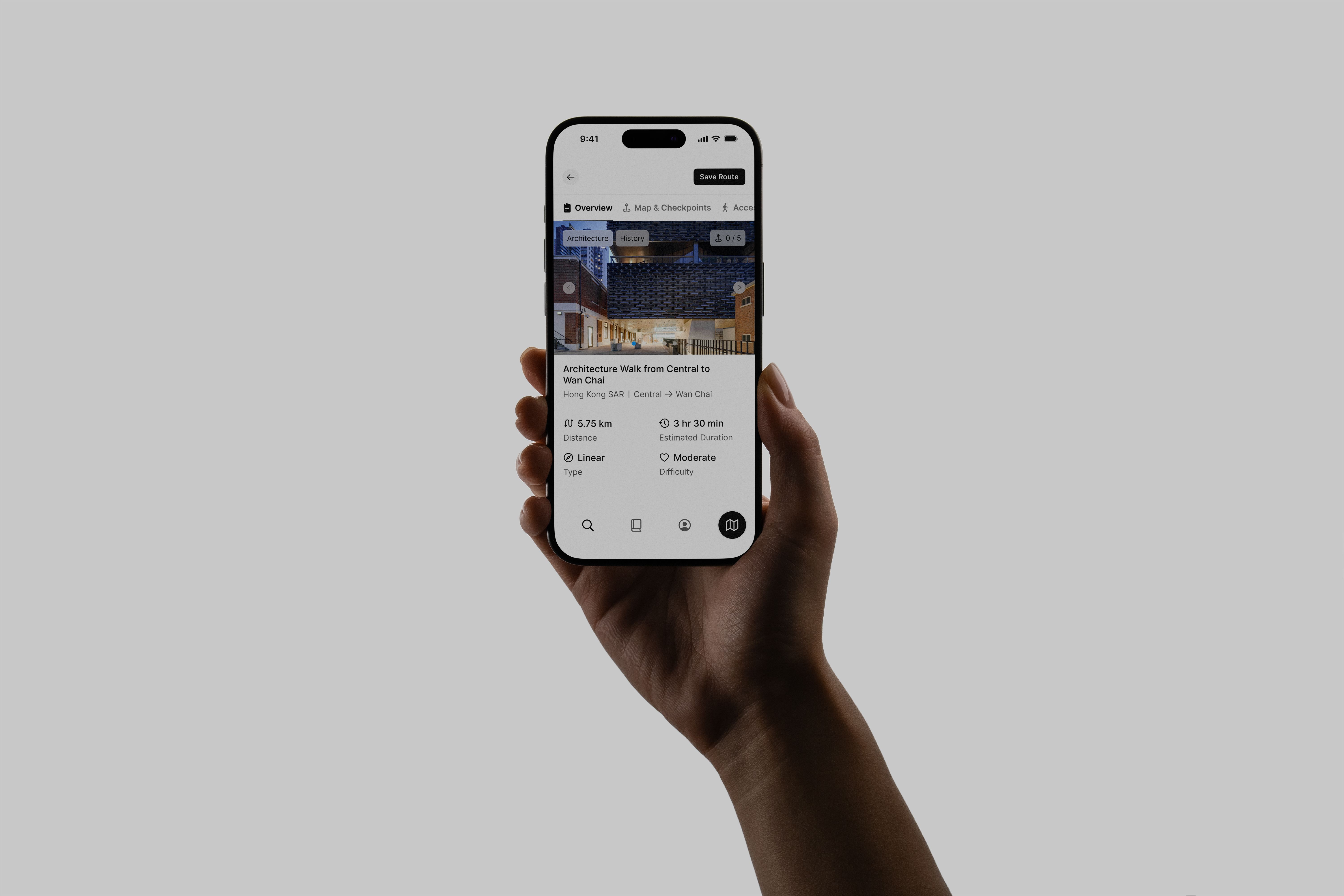 A person's hand holding an iPhone featuring the Many Roads app design on a metal desk.