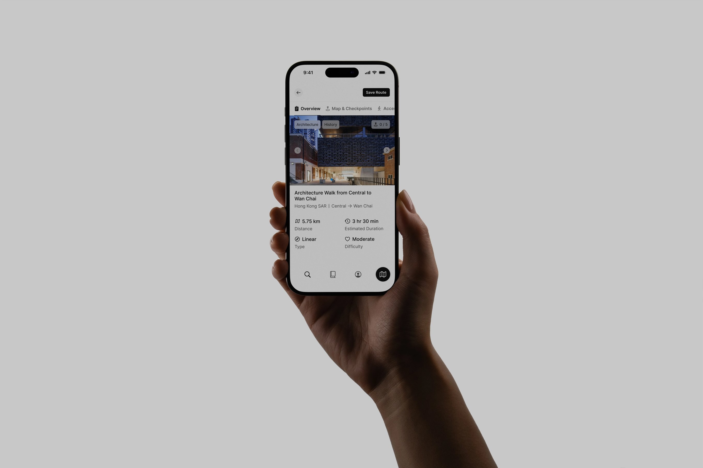 A person's hand holding an iPhone featuring the Many Roads app design on a metal desk.