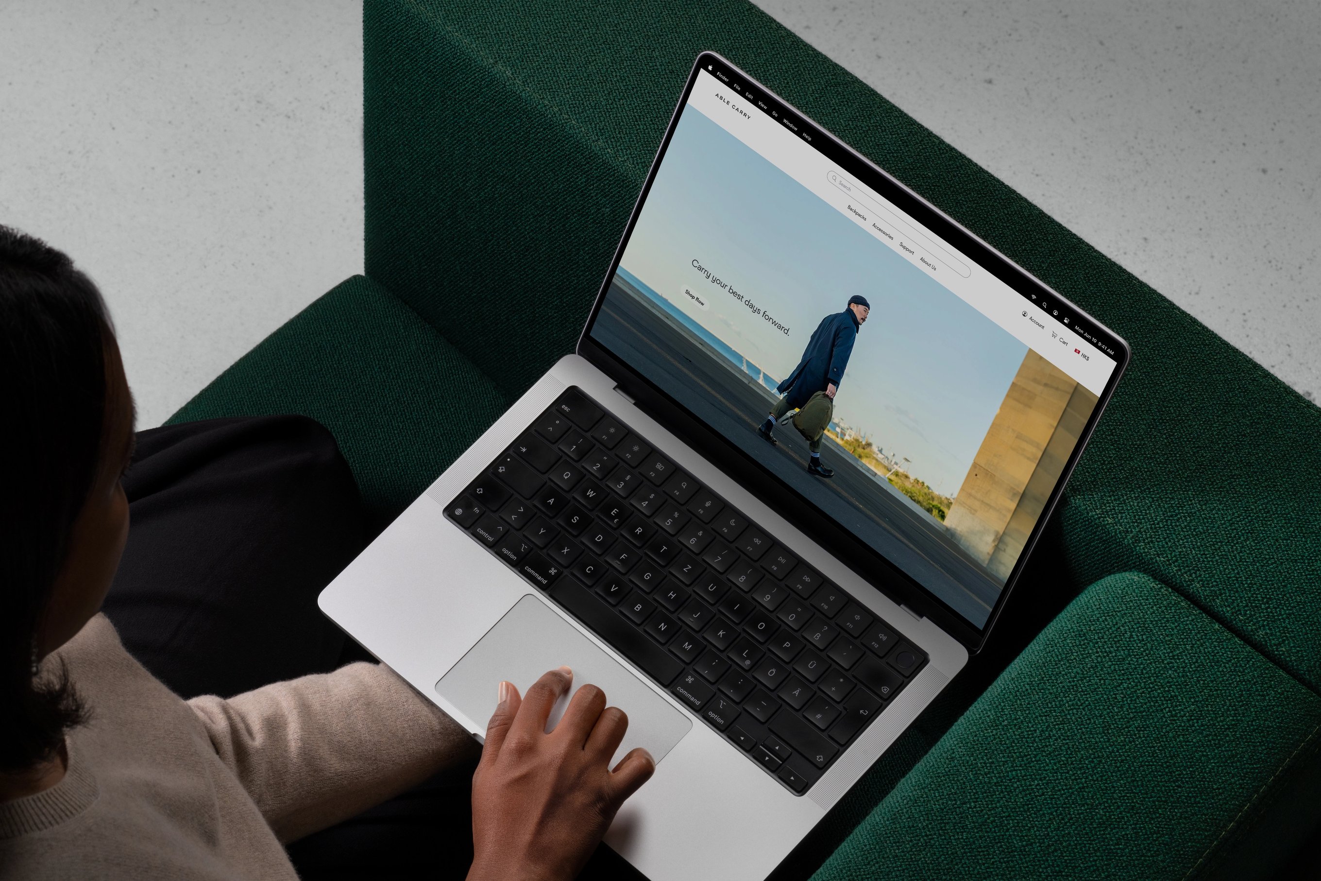 A woman sitting on a sofa with a MacBook Pro on her lap, viewing Able Carry's website on its monitor.