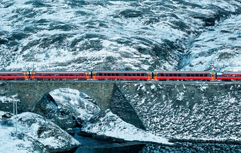 A train passing a lake in a snowy mountain landscape