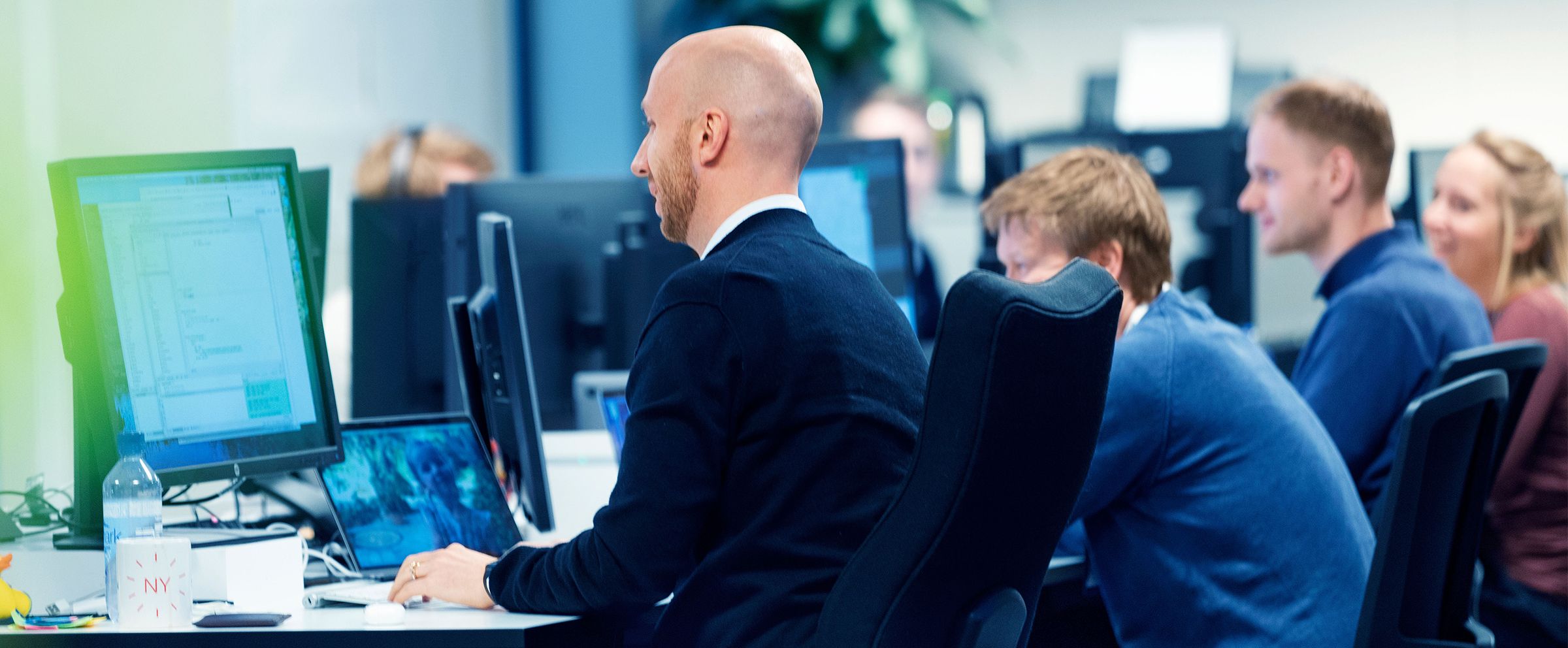 Bilde av en gruppe utviklere som sitter ved siden av hverandre på et kontor og jobber på pc-ene sine.