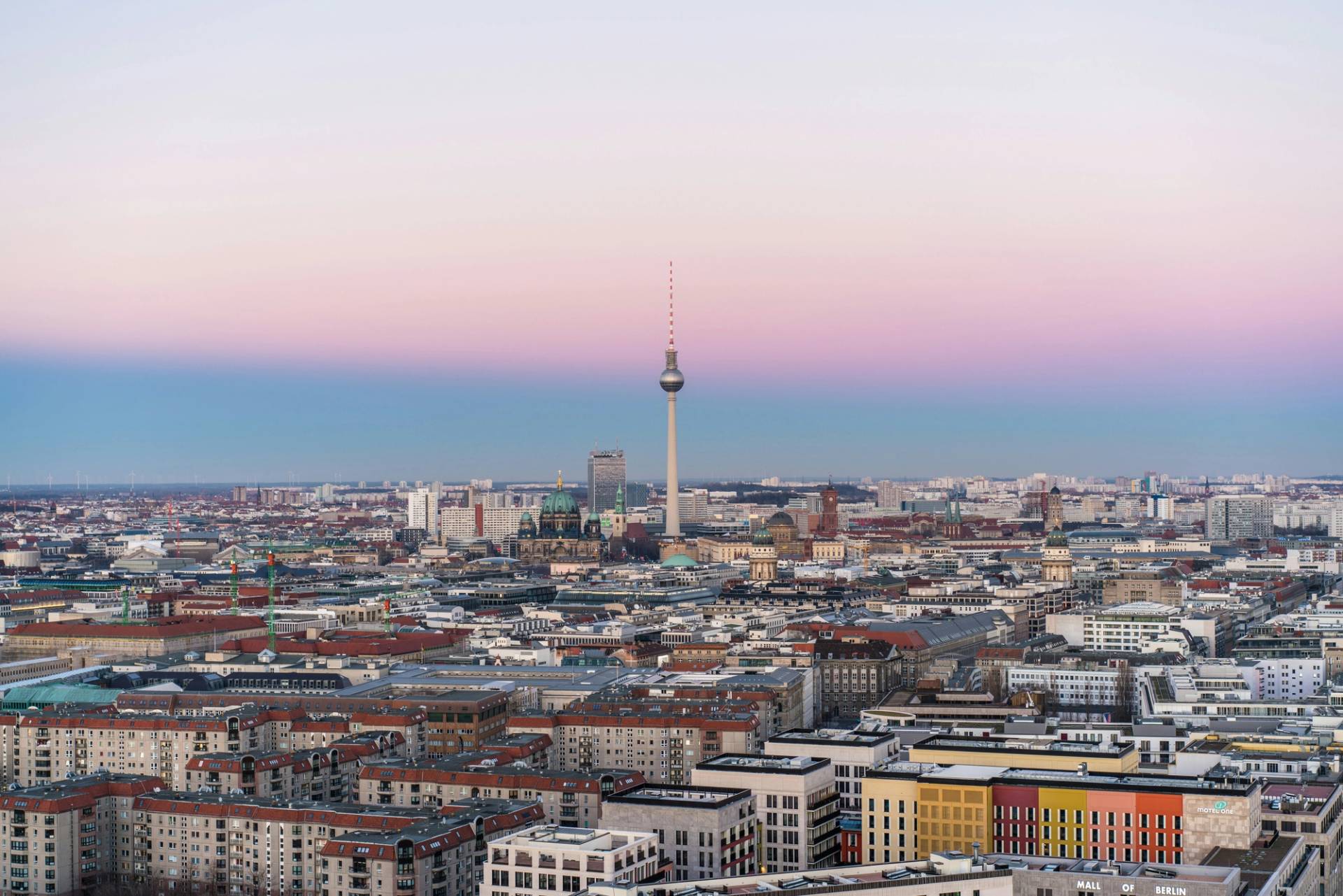 Utsikt over Berlin i skumringa med det ikoniske Fernsehturm-tårnet, Berliner Dom og taka i byen under ein rosa og blå himmel.
