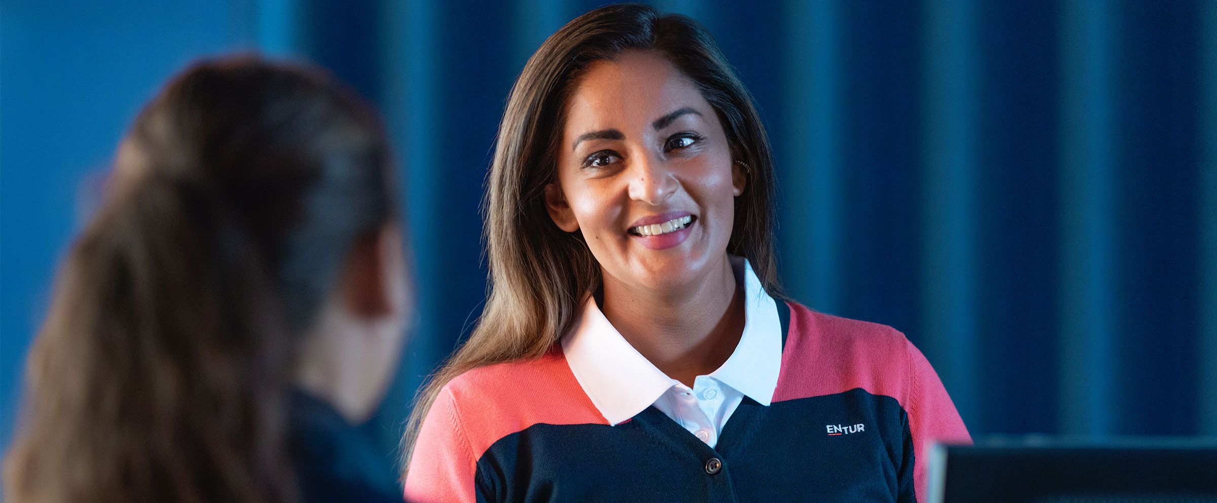 Bilde av Iram, en av Enturs ansatte på stasjoner. Hun smiler til en kunde som sees i forgrunnen av bildet.