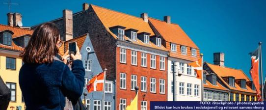 Situasjonsbilde av Nyhavn i København. I forgrunnen står en dame med ryggen til kamera. Hun holder opp telefonen sin, og det ser ut som hun tar bilde av gaten. 