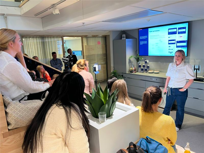 Bilde av en gruppe damer som sitter i en trapp og hører på en annen dames presentasjon.