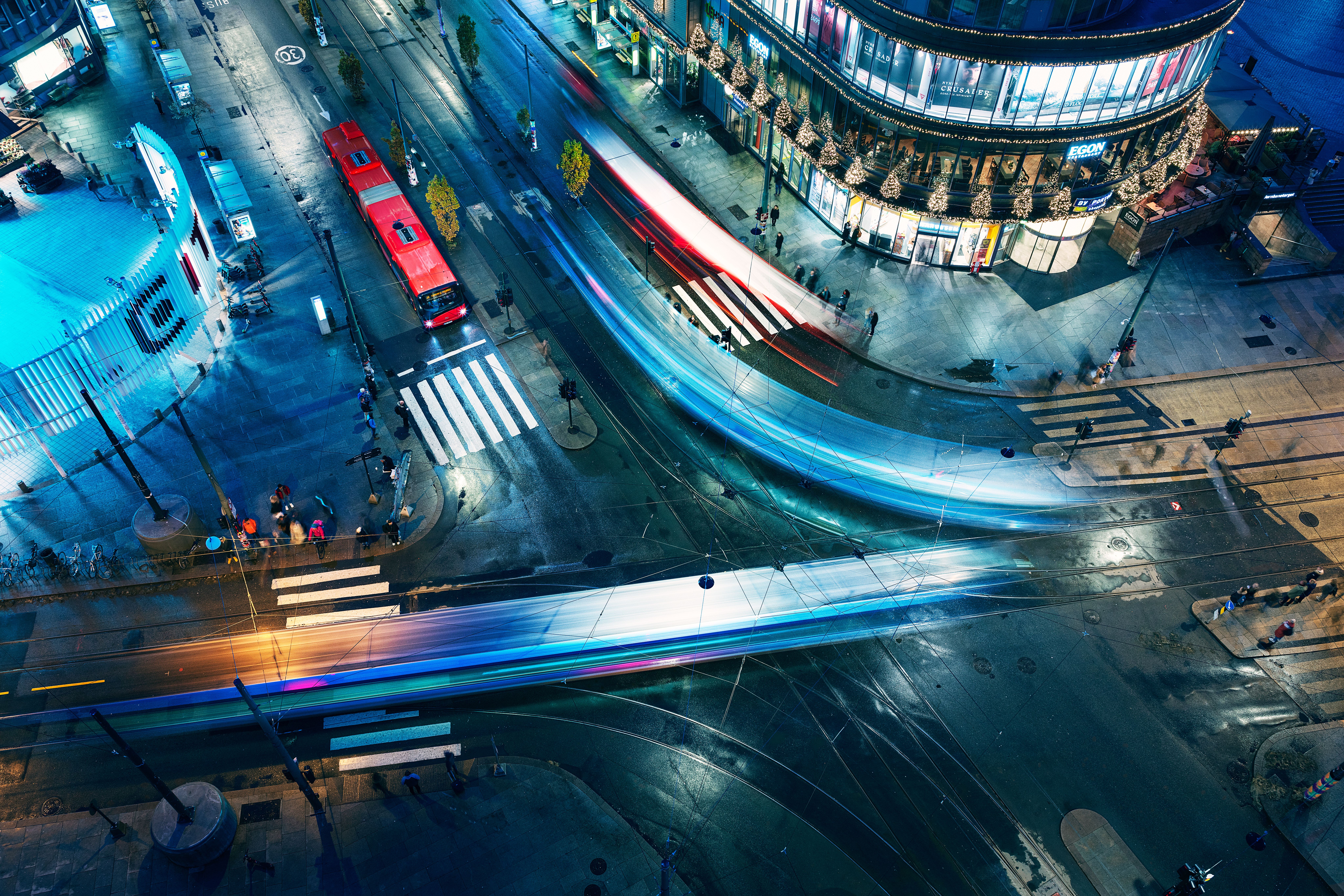 Bilde i fugleperspektiv av et lyskryss på natterstid med en rød buss kjørende på veien.