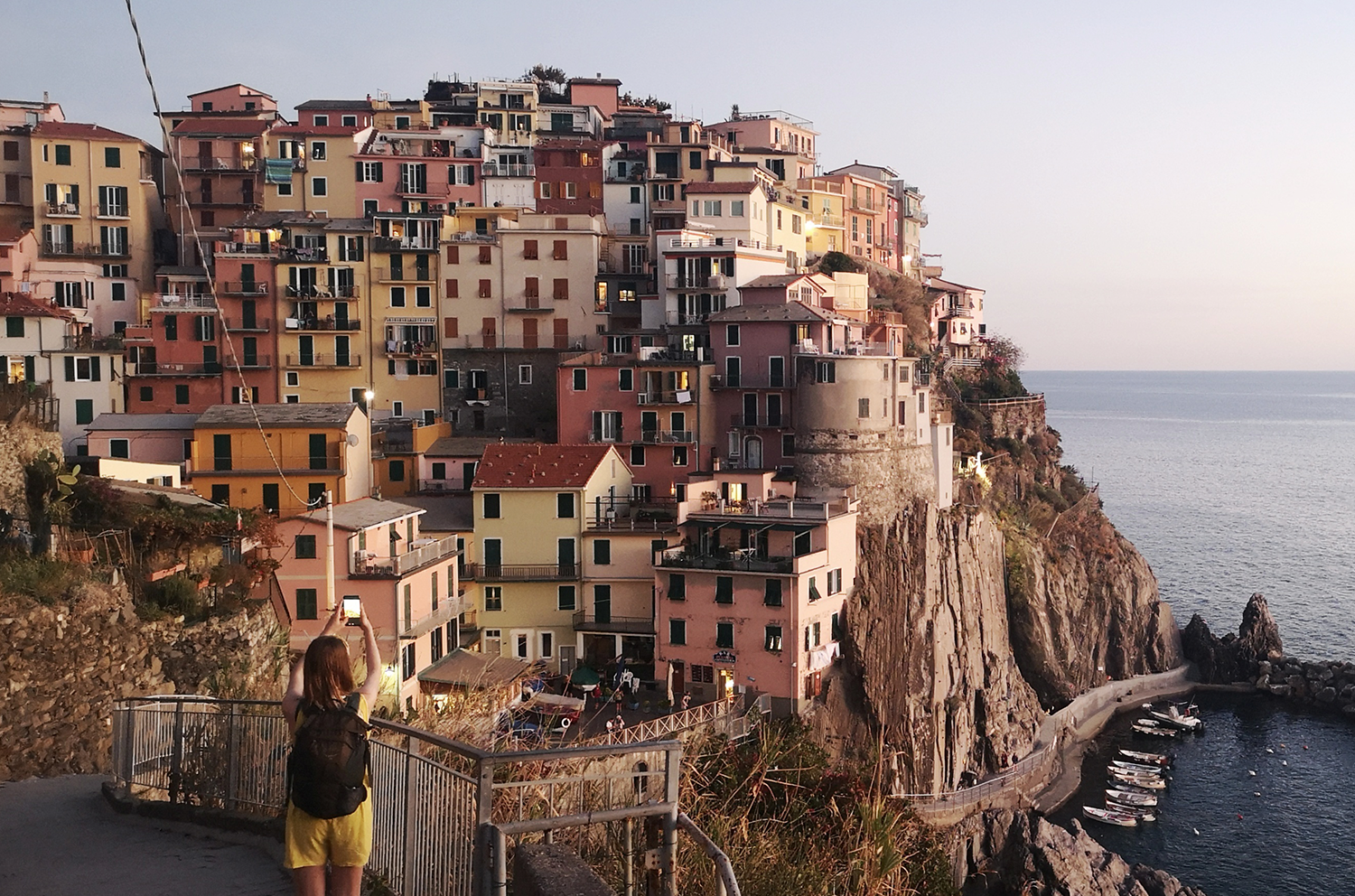 En pitoresk landsby ved sjøen i Italia. Datteren er i forgrunn med ryggen til og tar bilder med mobilen.