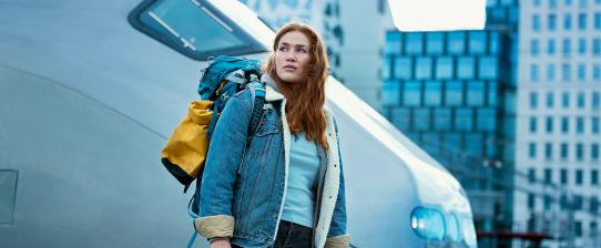 A woman with a backpack standing in front of a train. She seems ready to go on adventures. 