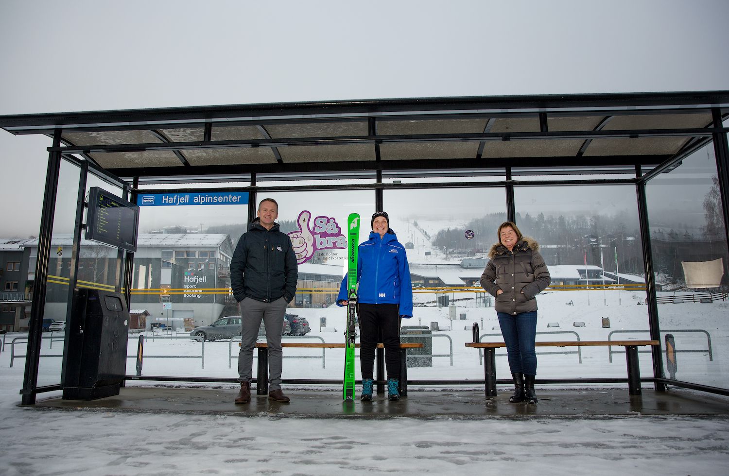 Bilde av Ove Gjesdal, Marit Lien og Stine Fredriksen som står inne i et busskur, hvorav Marit (i midten) holder et par alpinski.