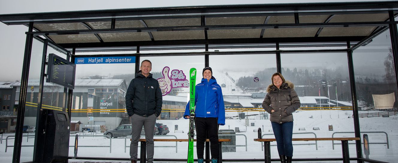 Bilde av Ove Gjesdal, Marit Lien og Stine Fredriksen som står inne i et busskur, hvorav Marit (i midten) holder et par alpinski.