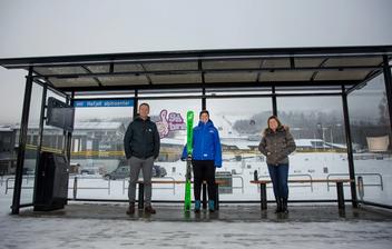 Bilde av Ove Gjesdal, Marit Lien og Stine Fredriksen som står inne i et busskur, hvorav Marit (i midten) holder et par alpinski.