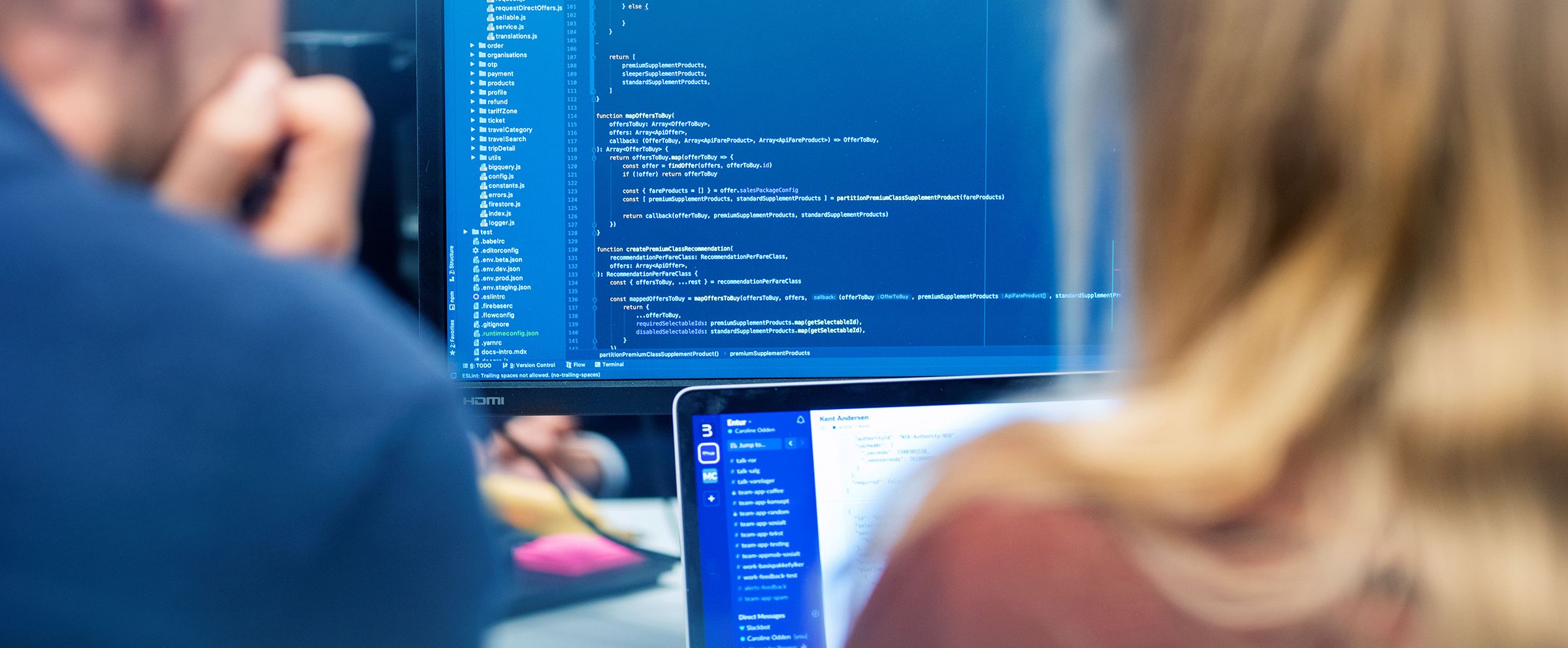 Bilde av to utviklere som sitter foran pc-skjermer som viser kodelinjer.