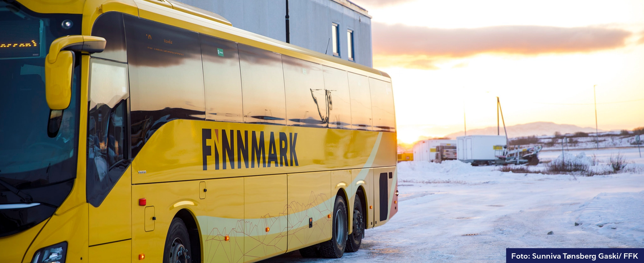 Bilde av et snødekt landskap og en rødmende himmel. Høyre side av bildet domineres av en gul buss med påskriften "Finnmark". 