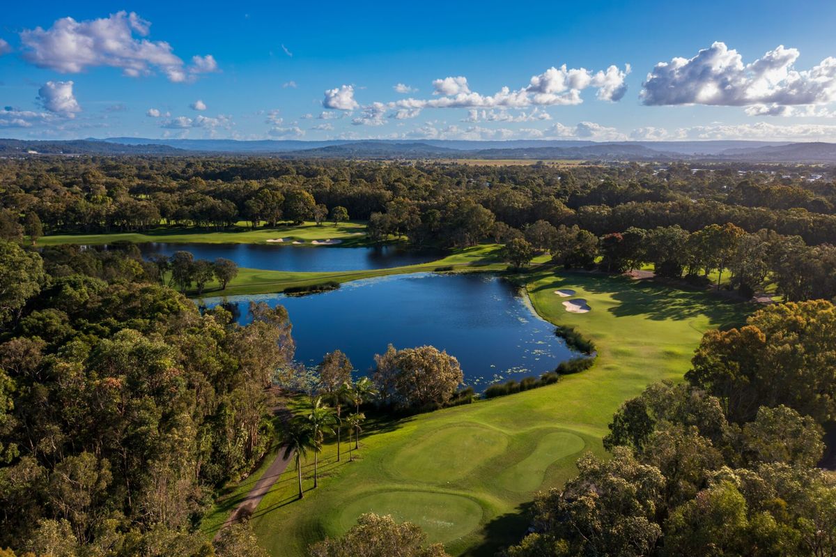 Aerial view of Twin Waters Golf Club showing a lake winding between fairways, bunkers, and palm trees.